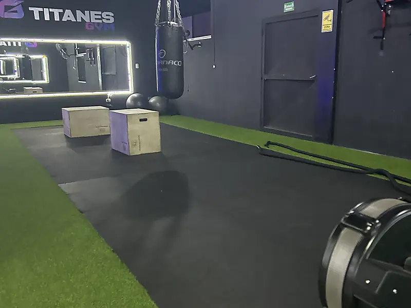 Zona funcional de Titanes Gym: cajones pliométricos, saco de boxeo y remadora sobre grama sintética