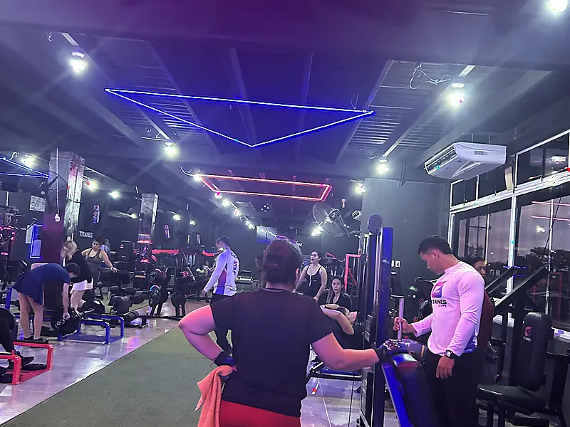 Atletas entrenando en la sala de pesas bajo aros de neón azul y rojo